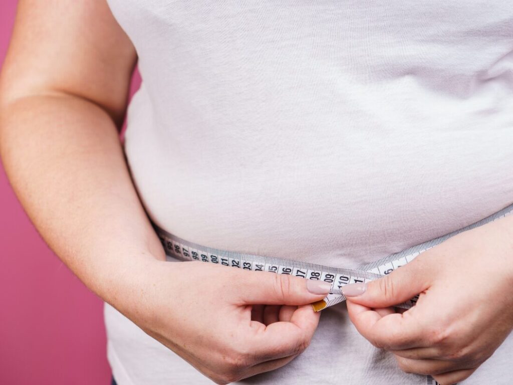 Woman measuring waist with pink tape measure for fat loss progress