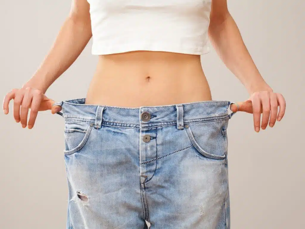 Woman showing weight loss progress holding out oversized jeans waistband